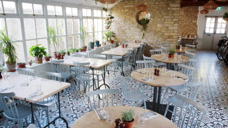 mesas redondas y sillas azules de huevo de pato en un restaurante vacío con azulejos de piso con patrones y plantas de interior que crecen en el alféizar de la ventana