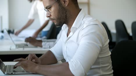 side view of thoughtful male worker using laptop.