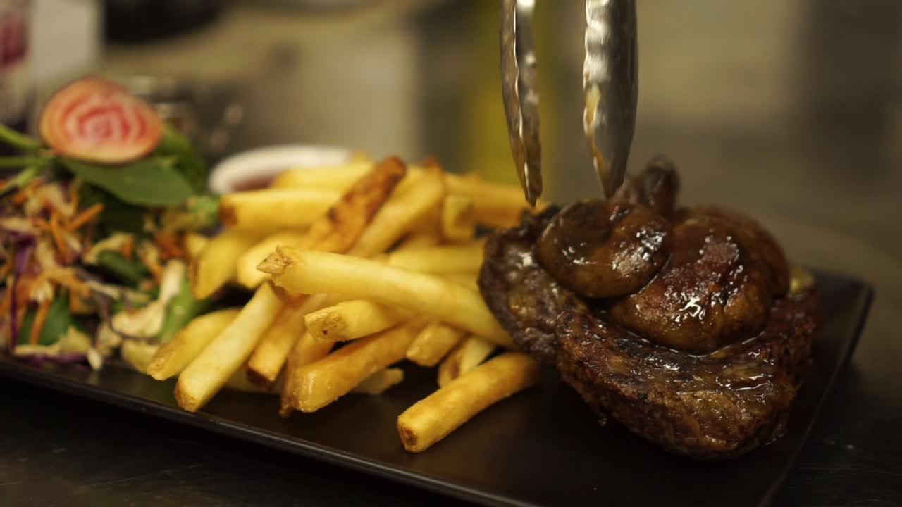 primer plano - terminando la presentación de filete de ternera a la parrilla, salsa, champiñones, papas fritas crujientes doradas y ensalada verde en un plato negro