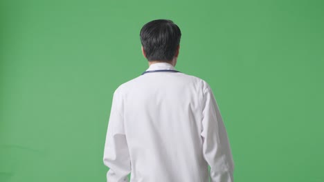 back view of asian male doctor with stethoscope walking on green screen background in the hospital