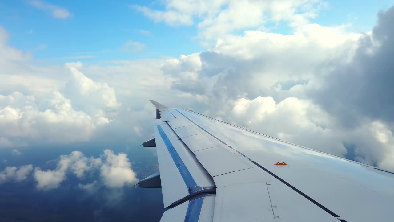 The stunning sight from an airplane wing as it soars high above the ocean. The bright blue sky is dotted with fluffy white clouds, creating a serene landscape