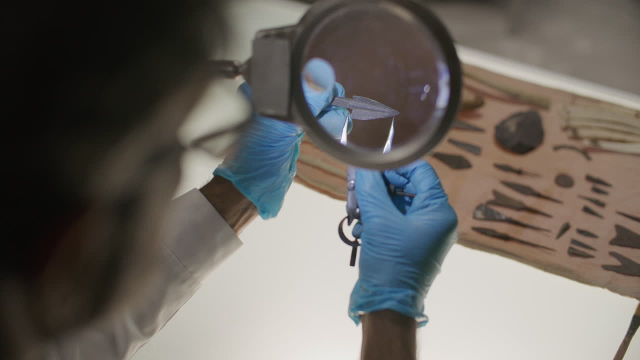 Archaeologist Measuring Ancient Arrowhead under Magnifying Glass in Lab