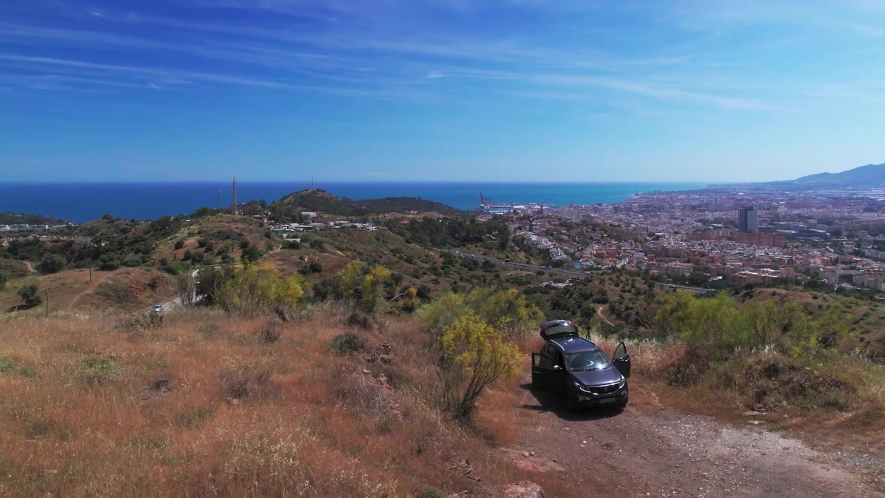 Colline circostanti Malaga di giorno, ripresa aerea che si muove in circolo per rivelare la città e un'auto SUV su una strada sterrata, Andalusia, Spagna.