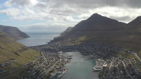 vuelo de drones hacia atrás que muestra la bahía y la ciudad costera de klaksvik en la isla feroe durante el día soleado y nublado - área de vivienda y arquitectura alrededor de la bahía del río en la isla de bordoy