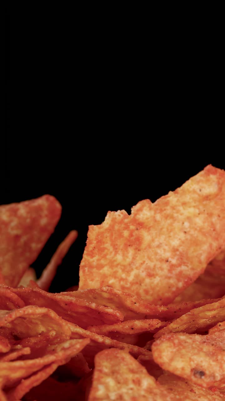 Croccanti patatine tortilla cadono su un mucchio, riprese al rallentatore con un'illuminazione da studio drammatica.