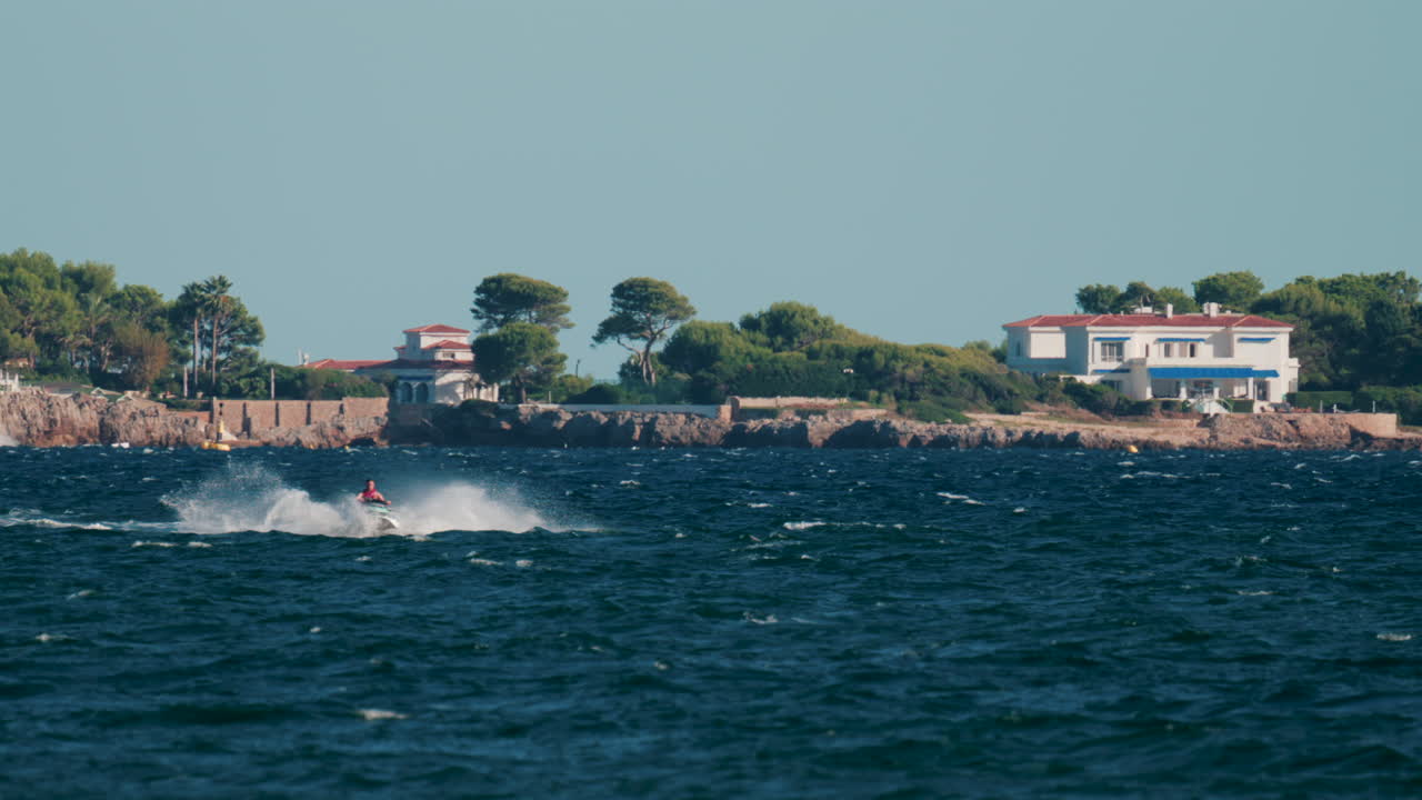 Cannes, France - October 4, 2025: Black speed boat creating splashes while racing on deep blue sea near rocky coastline and luxury villas