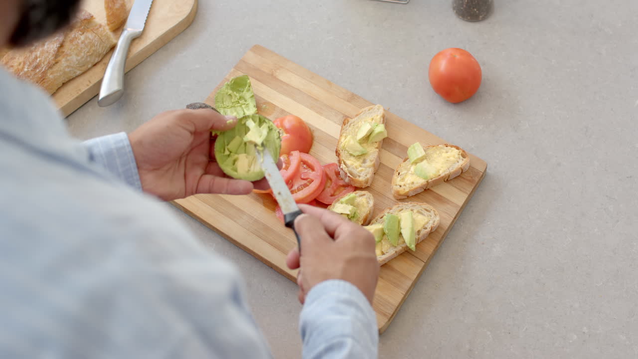Preparing avocado toast, man spreading avocado on bread slices in kitchen