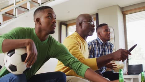 African-american-father-and-twin-teenage-sons-sitting-on-couch-watching-game-on-tv-and-talking