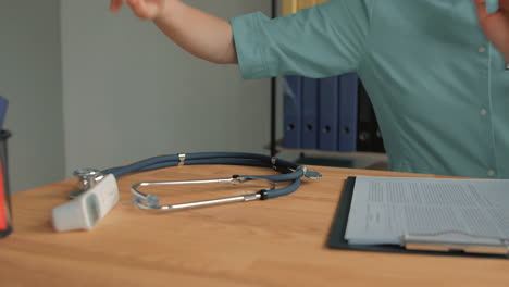 young pretty blonde female nurse care taker working at the office desk, picking up stethoscope and clipboard