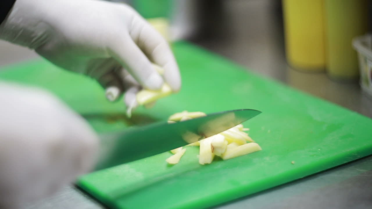 Hand Cutting The Potatoes In The Kitchen. Hand with a knife cutting the potatoes on the board in the kitchen