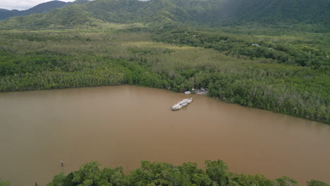 el ferry parte en el delta, el paisaje de aguas marrones, las colinas boscosas, el río daintree, la vista panorámica aérea del dron.