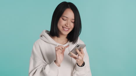 asian woman texting on smartphone and laughing on camera.