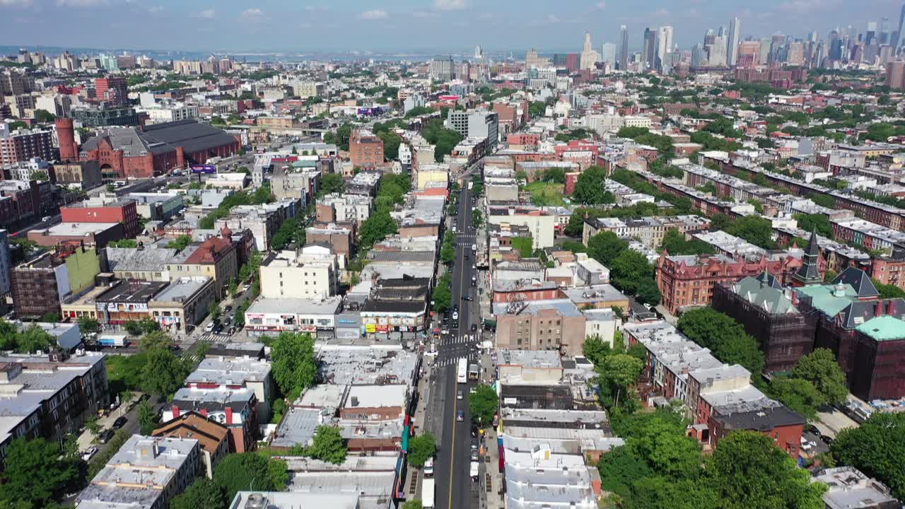 An aerial view over Bedford Stuyvesant, Brooklyn. The drone camera travels over Fulton Street and slowly pans upward to reveal the Manhattan skyline and the blue skies above.
