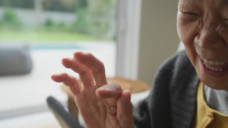 una abuela asiática riendo usando un teléfono inteligente y una nieta adulta llegando por la puerta trasera