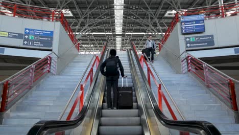 traveler with suitcase on escalator in modern airport terminal with signs and red railings