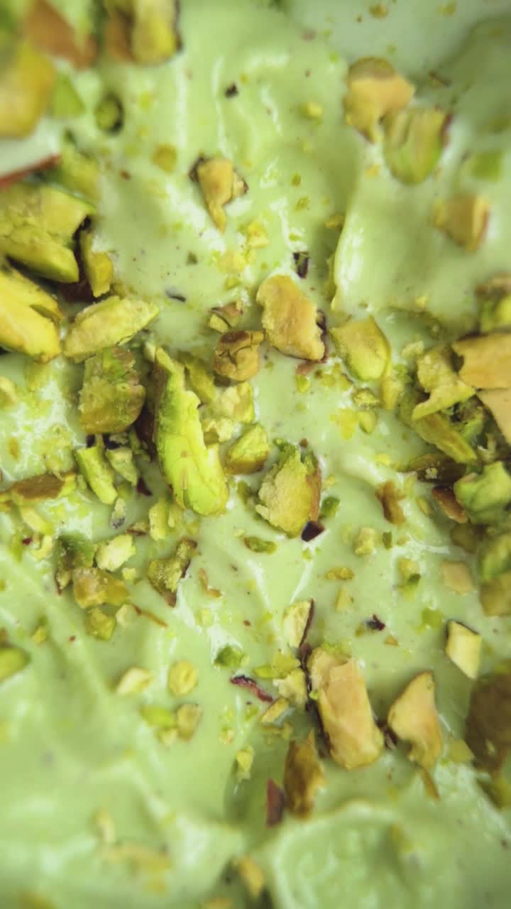 Vertical footage focusing on the smooth green surface of pistachio ice cream topped with whole raw pistachios. A treat for dessert lovers