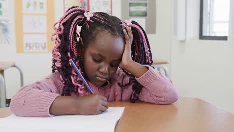 in classroom, young girl concentrating on writing in notebook, deep in thought, at school