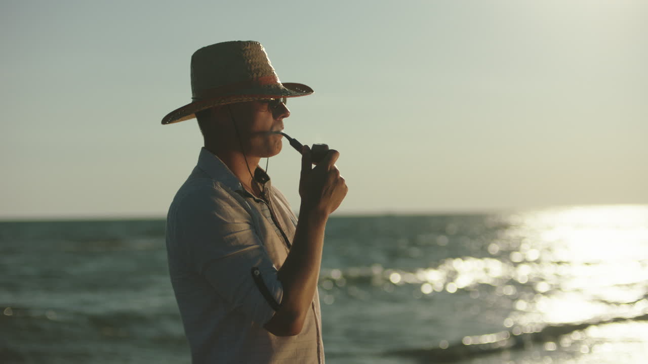 Uomo che fuma la pipa su una spiaggia al tramonto