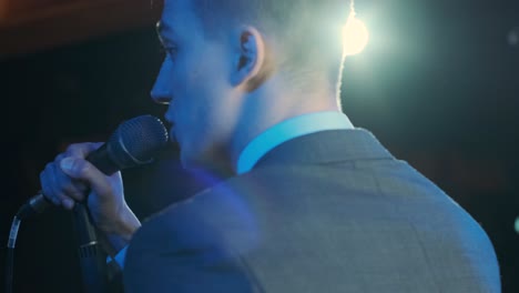 man singing song in microphone during performance on stage on rock concert. close up man rock star singer on music concert on colorful light background