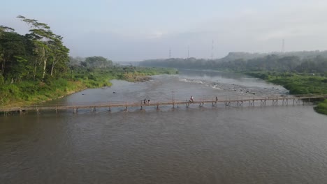 aerial footage shows a wooden bridge spanning the progo river, passable by motorbikes. as a link between the villages of bantul and kulonprogo.