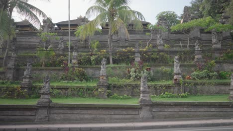 ancient balinese temple wall with stone statues and a cyclist on the road