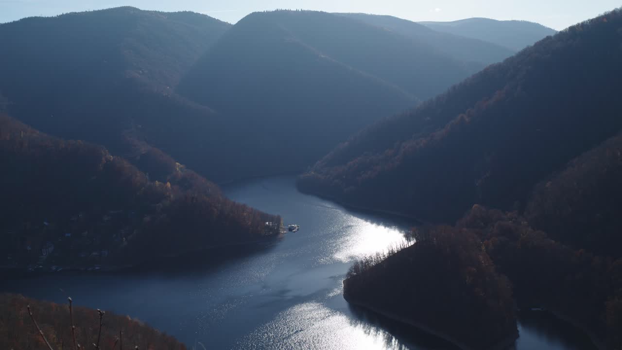 Shot of a majestic river gorge carving its way between towering, forested mountains. Sunlight glints brightly on the reflective water. Conveys a sense of nature, travel, and adventure