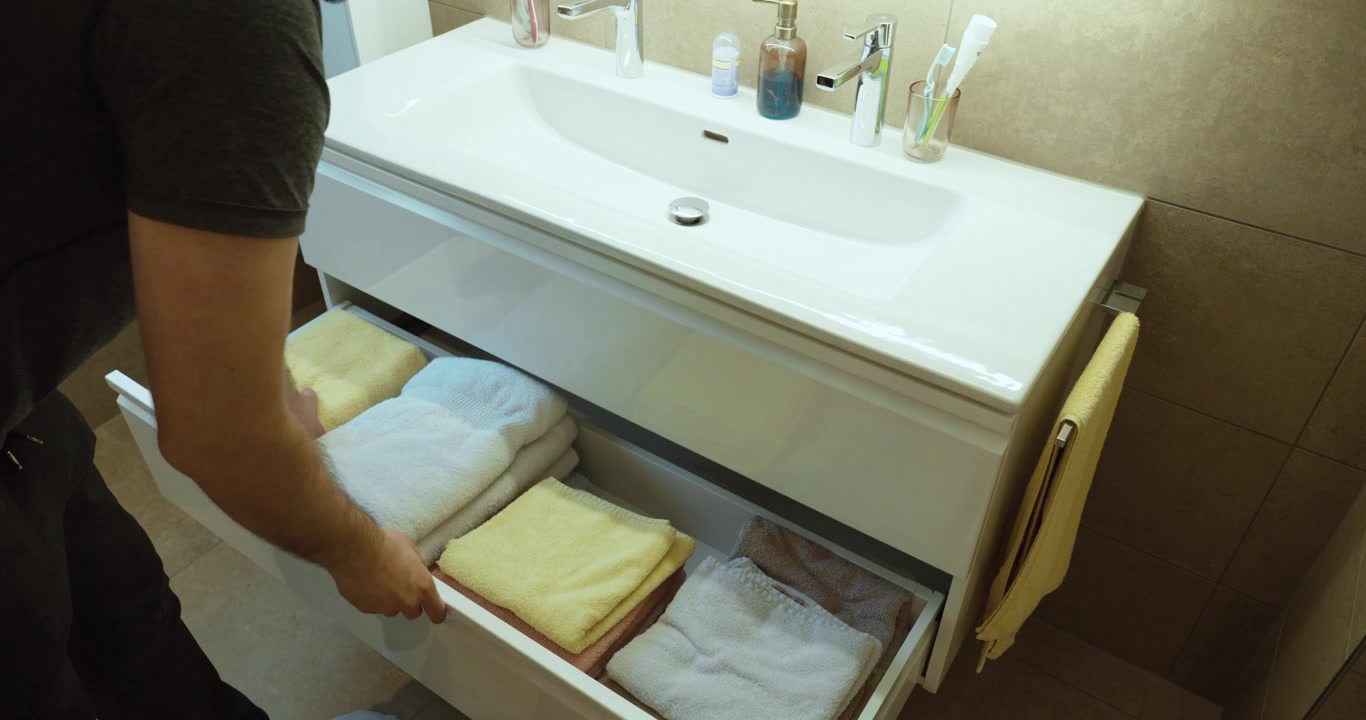 Person opening a bathroom vanity drawer and arranging clean folded towels inside. Concept of household organization, bathroom storage, cleanliness, home management, personal hygiene, laundry, and dome