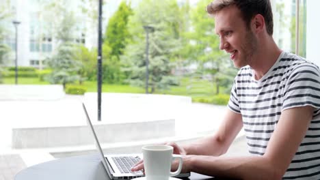 un estudiante sonriente bebiendo café y escribiendo en una computadora portátil