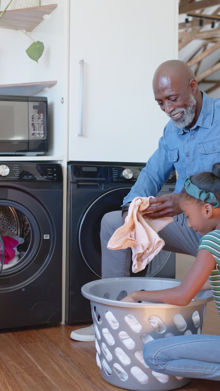 Vertical video: Senior man sorting while child handing clothes from bin into washer at home