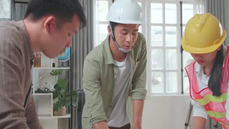 three asian engineers with helmets presenting work to a man at the office