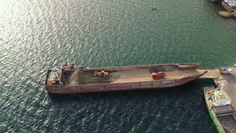 cargador y volquetes que transportan y cargan arena en una barcaza anclada en el puerto