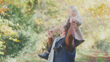 father playing game carrying daughter on shoulders on family walk along track in autumn countryside