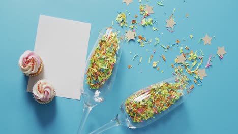 Champagne glasses with confetti and white card on blue background at new year&#039;s eve