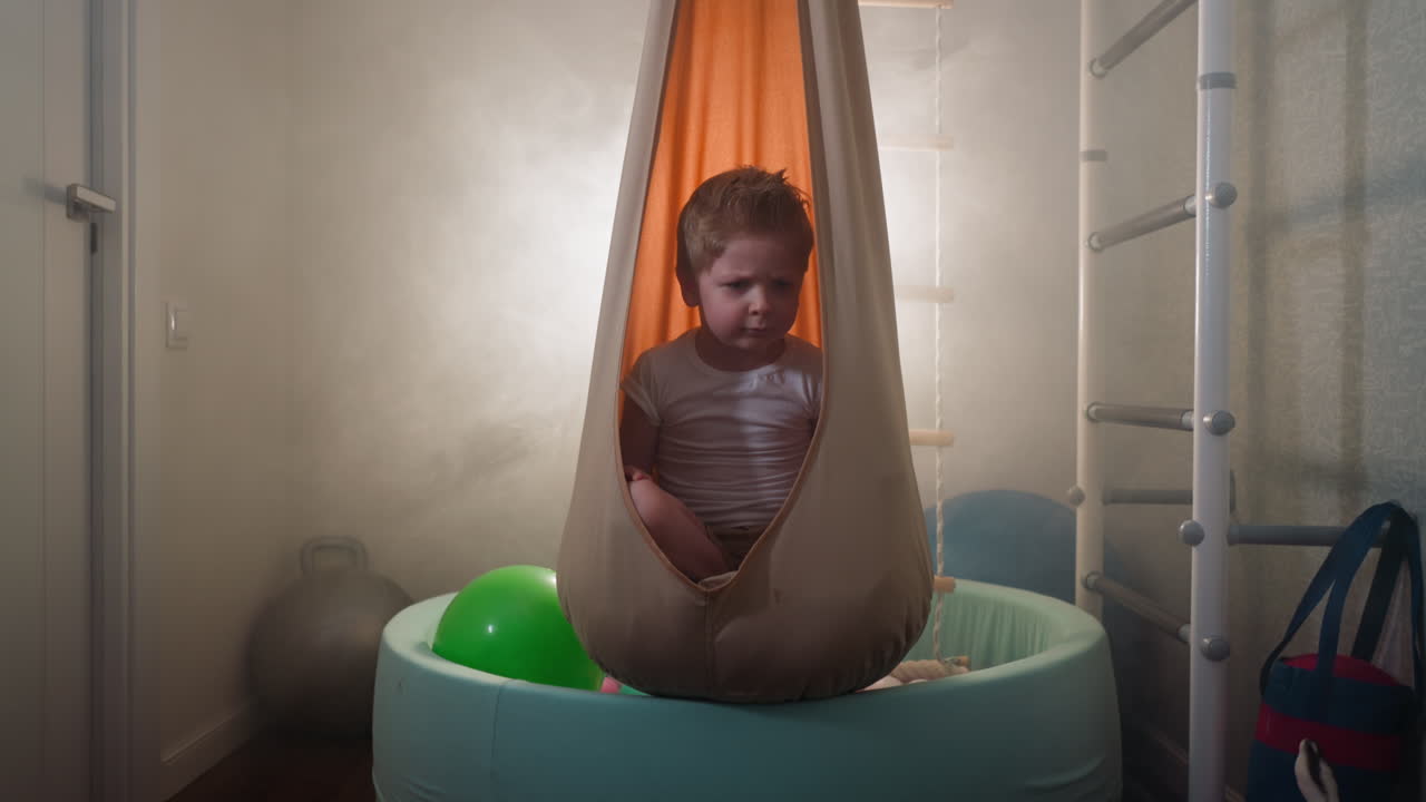 귀여운 금발 유아는 집 체육관에서  ⁇ 으로 머리를 움직여 눈살을  ⁇ 푸린다