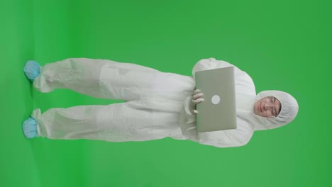 full body of asian man wearing personal protective equipment uniform ppe holding and working with laptop computer in the green screen studio