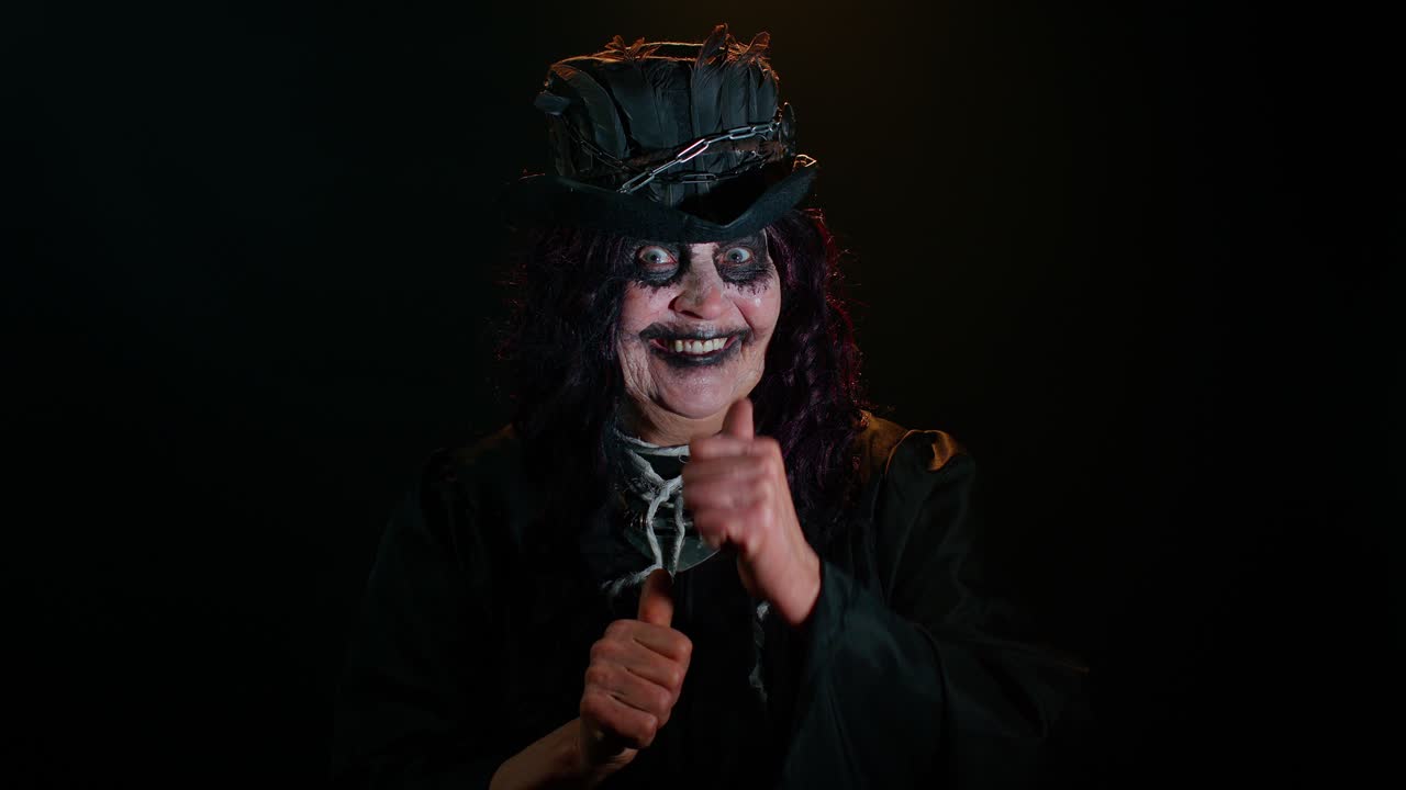 una anciana siniestra con un aterrador maquillaje de bruja de halloween en disfraz levanta el pulgar como un gesto