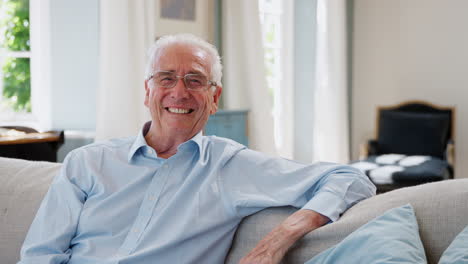 Portrait-Of-Smiling-Senior-Man-Sitting-On-Sofa-At-Home
