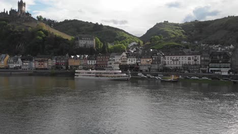 drone despega con vistas a la ciudad de cochem y un barco fluvial junto a la orilla del río,