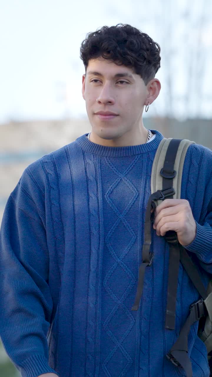 Young latino student walking outdoors with backpack. Vertical