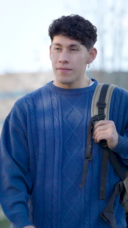 young latino student walking outdoors with backpack. vertical
