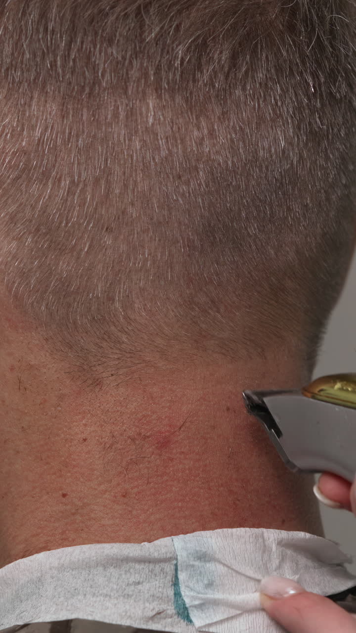 Primo piano di un uomo a cui vengono rifiniti i capelli sulla nuca con un tagliacapelli elettrico