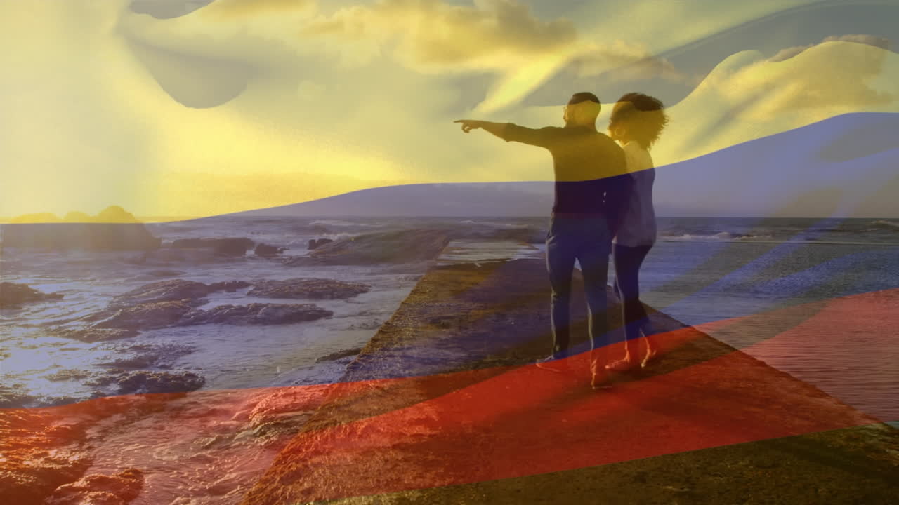 Animation of waving colombia flag over african american couple walking together on the promenade