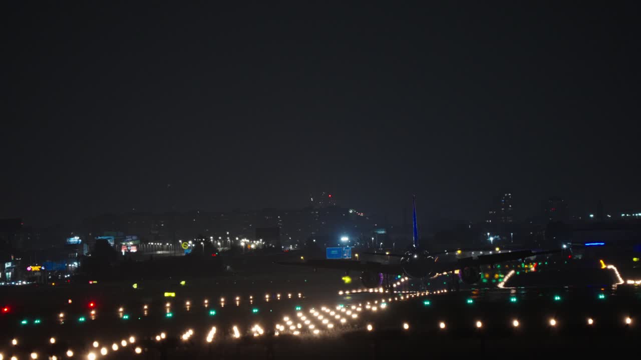 夜のライトアップされた滑走路に着陸する民間航空機