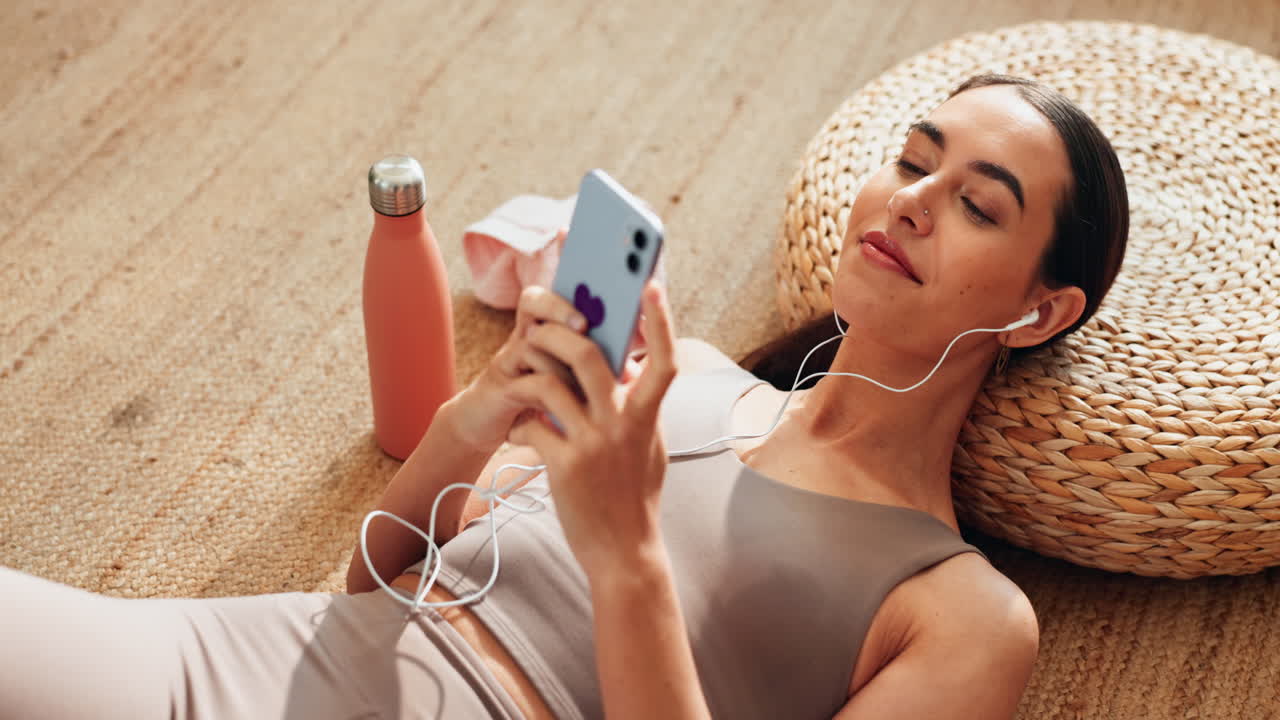 운동 후에 휴식을 취하고, 드폰으로 음악을 듣고 있는 여자.