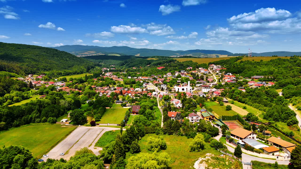 Daytime village scenery in Europe. A quaint village is set amid lush greenery and hills under a bright blue sky, highlighting rural European life