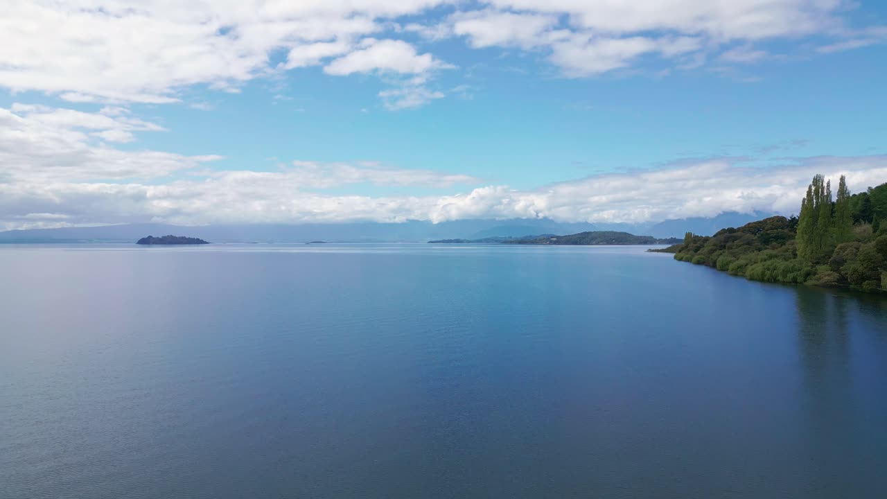 島々と森林に覆われた岸辺がある穏やかな湖の上空を前方へ飛行。チリ、ラゴ・ランコ。