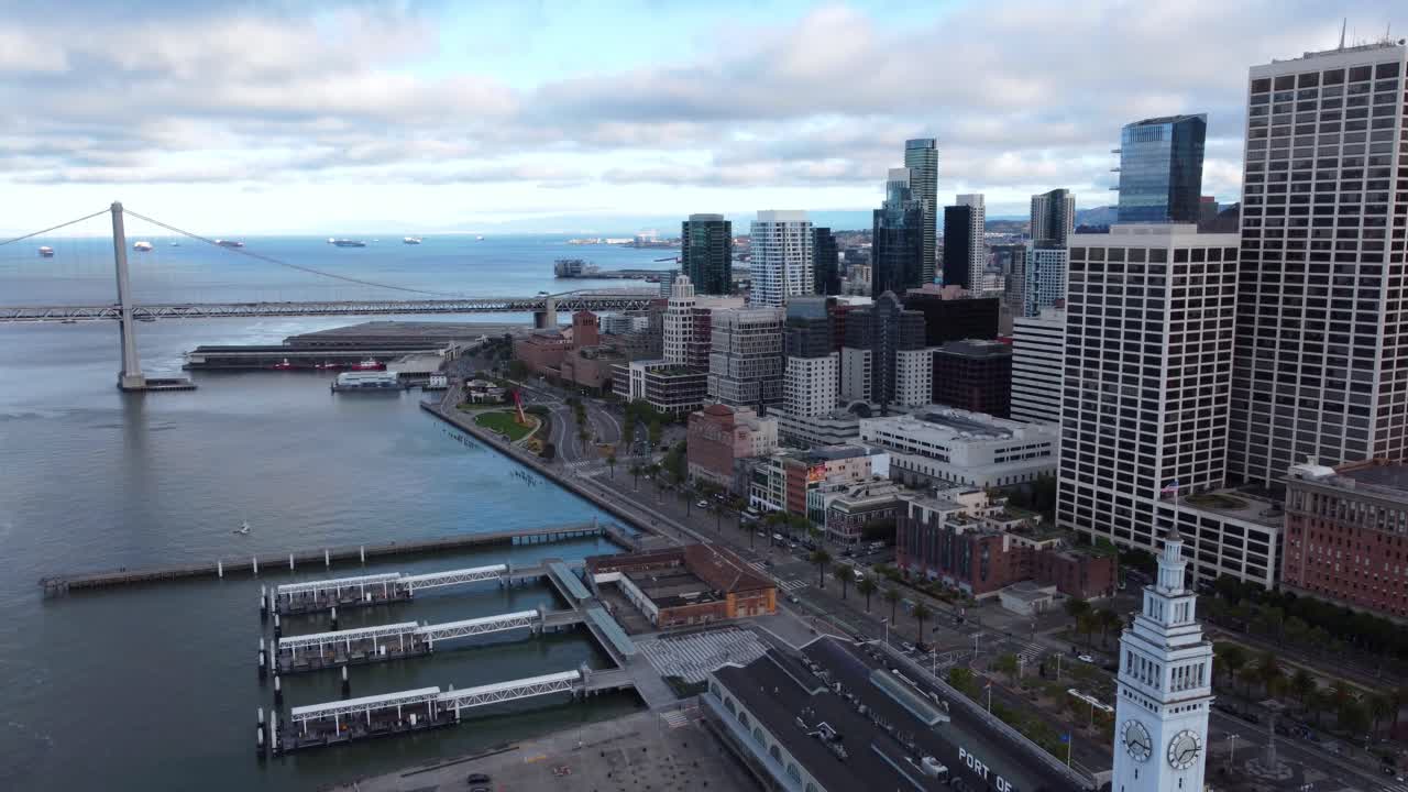 4K 30fps Aerial Drone Footage of San Francisco City Skyline and the Oakland Bay Bridge - Cars Travel Along the Highway, Calm Cloudy Day, Water Ripples, Port of San Francisco, Piers and Harbors