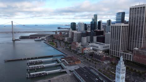 4k 30fps aerial drone footage of san francisco city skyline and the oakland bay bridge - cars travel along the highway, calm cloudy day, water ripples, port of san francisco, piers and harbors