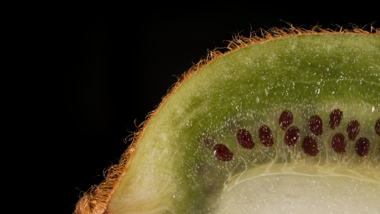 una rebanada macro de kiwi verde fresco y semillas de fruta sobre un fondo negro. una juicosa fruta de kiwi fresca, madura y deliciosa, cortada en rodajas, de primer plano.