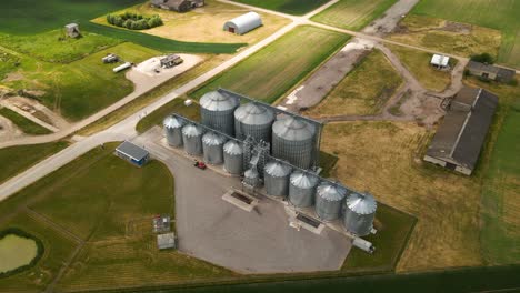 Drohnenansicht-Des-Agro-Silos-Turms-Zur-Lagerung-Landwirtschaftlicher-Produkte-Und-Getreidesilos-Inmitten-Eines-Grünen,-Bewirtschafteten-Feldes